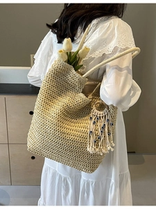 Woven straw tote bag with evil eye tassel charm held by model in white lace dress