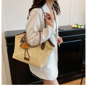 Detail of woven straw tote bag with brown handles and a cute bear charm on a female model
