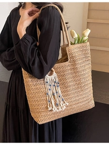 Large woven straw tote bag with evil eye tassel charm shown on a female model shoulder