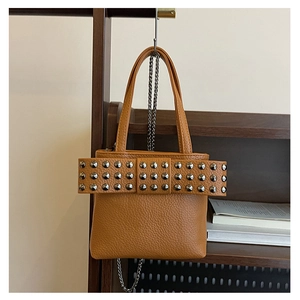 Détail du sac seau en cuir marron avec nœud à rivets et bandoulière chaîne argentée