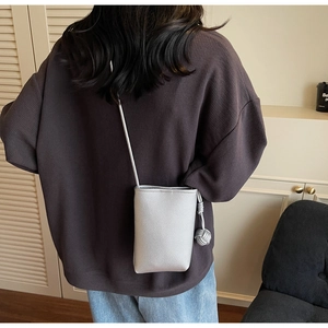 Silver pebble leather mini crossbody phone bag with woven ball charm shown on a model