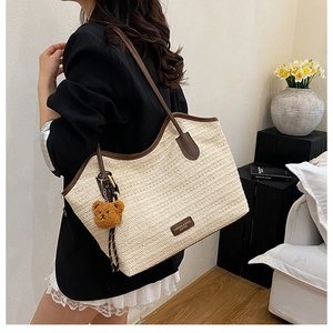 Detail of woven straw tote bag with brown leather trim and a cute plush bear charm