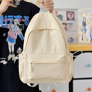 Dettaglio dello zaino in nylon crema con tasca frontale a zip e logo GDMNQ ricamato