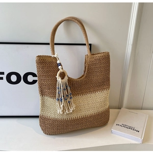 Detail of striped straw tote bag featuring decorative fringe and evil eye bead charm