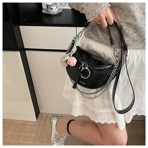 Detail of black saddle bag with silver chain, woven knot charm, and adjustable strap