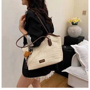 Detail view of woven straw tote bag with brown leather handles and a cute bear charm