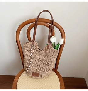 Detail view of woven straw tote bag with brown leather handles and a white rope charm