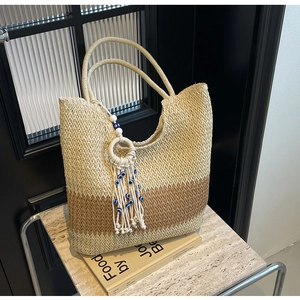 Detail of V-shaped woven straw tote bag featuring bohemian tassels and evil eye bead