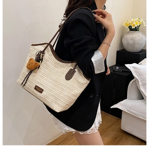 Close-up of woven straw tote bag with brown leather trim and a plush bear pendant