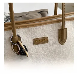Dettaglio borsa tote color crema con manici marroni e ciondolo a forma di orsetto