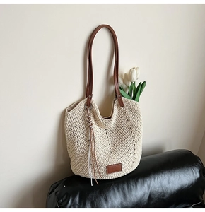 Detail of woven straw tote bag with brown leather handles and decorative tassel accent