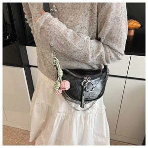 Detail of black saddle crossbody bag with silver chain and colorful woven ball charm