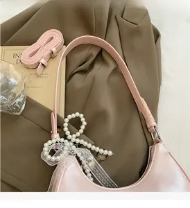 Detail der rosa perlmuttfarbenen Sichel-Tasche mit Perlenanhänger und Spitzenschleife