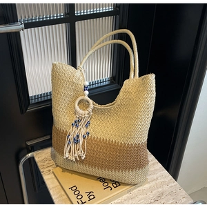 Detail of woven straw tote bag featuring two-tone design and blue evil eye tassel charm