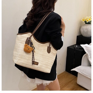 Detail of woven straw tote bag with brown leather trim and hanging plush bear charm