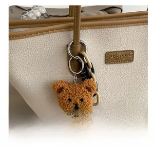 Dettaglio di un ciondolo a forma di orsetto marrone con corda su borsa tote in pelle bianca