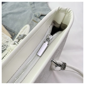Close-up of white snake pattern tote bag featuring smooth metal zipper and pearl handle detail