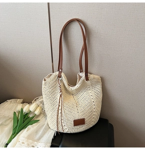 Close-up of woven straw tote bag texture with brown leather handles and tassel detail