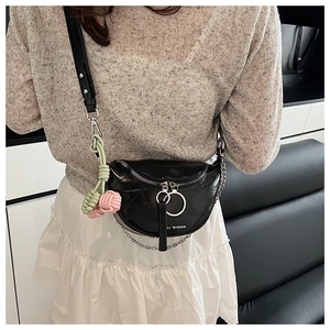 Detail of black leather saddle bag with chain strap and colorful woven charm on a model