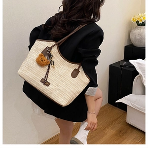 Detailed texture of the woven tote bag with brown leather straps and a plush bear charm
