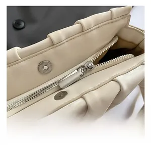 Close-up of metal zipper and magnetic snaps on cream pleated dumpling shoulder bag