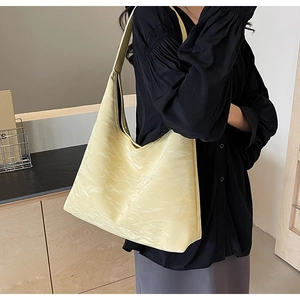 Detail of light yellow textured leather tote bag worn by a model in a minimalist setting
