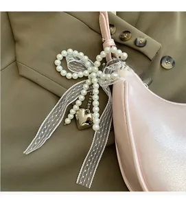 Detail eines Perlen-Schleifenanhängers mit Spitze und Herz an einer rosa Tasche