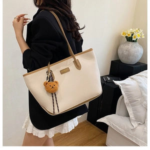 Dettaglio di una borsa tote minimalista con ciondolo a forma di orsetto e logo in metallo
