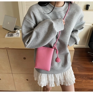 Detailed close-up of a pink textured mobile phone bag with a woven ball charm decoration