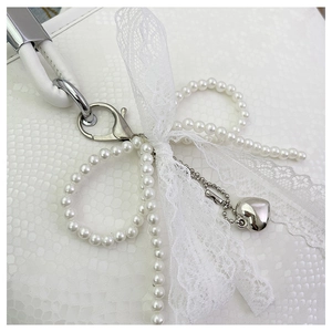 Close-up of pearl bow pendant with lace ribbon and silver heart on a tote bag