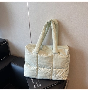 Detailed view of light green quilted down tote bag on minimalist studio background