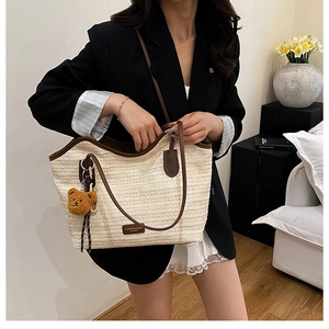 Detail of woven straw tote bag featuring brown leather trim and cute plush bear charm