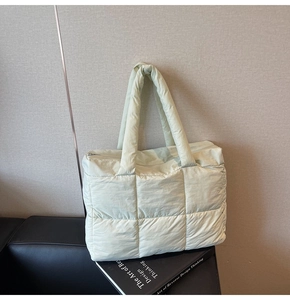 Close-up of pale green quilted down tote bag featuring square texture and metal zipper