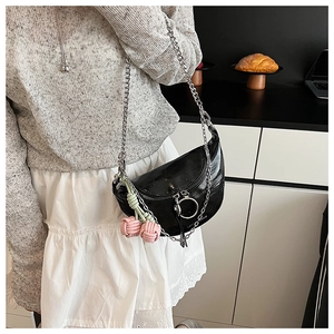 Detail of black saddle bag with silver chain strap and knit cherry charm on a model