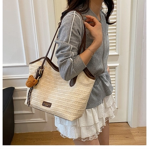 Close-up of woven straw tote bag featuring brown leather trim and a cute teddy bear charm