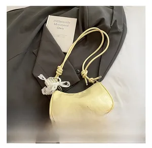 Detail of creamy yellow pleated bag with white lace pearl bow on grey blazer and book