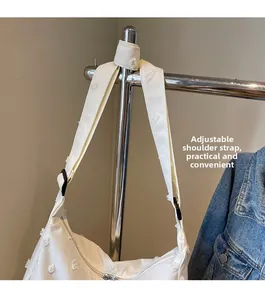 Detail showing white canvas tote with tassel texture and adjustable black shoulder strap