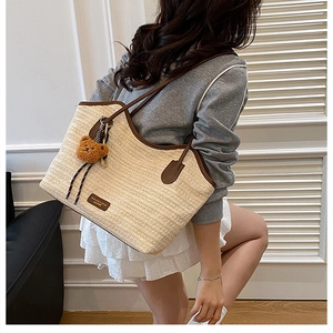 Detail view of woven straw tote bag featuring brown leather trim and a cute plush bear charm