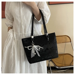 Close-up of black tote bag with snakeskin texture and pearl bow charm detail