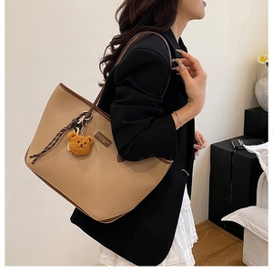 Dettaglio borsa tote in pelle marrone con etichetta logo e ciondolo a forma di orsetto