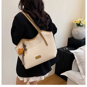 Detailed view of cream tote bag with brown leather trim and cute teddy bear charm
