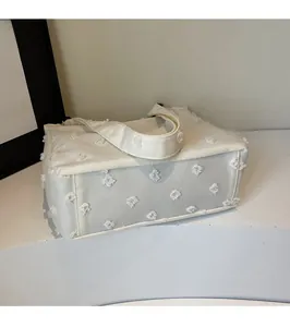 Detailed macro view of the frayed floral texture on this white canvas tote handbag