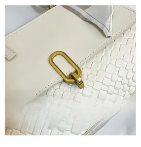 Detail of woven texture on beige handbag featuring a matte gold clasp and decorative silk scarf