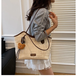 Close-up of woven straw tote bag with brown leather trim and cute teddy bear charm detail