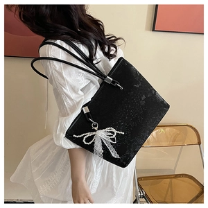 Macro detail of black snake-pattern tote bag with pearl bow and white lace charms