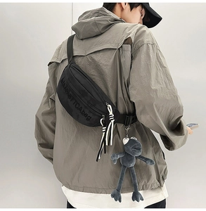 Detail of black nylon chest bag with letter embossing and a plush frog pendant