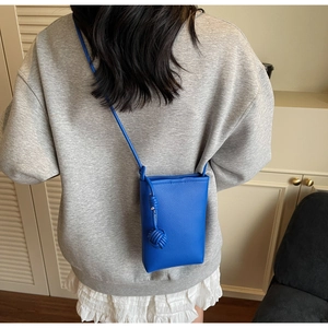 Lychee texture bright blue crossbody phone bag with woven ball pendant on a model
