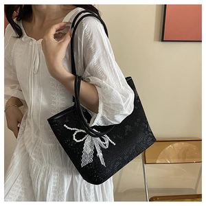 Detail of black faux-snakeskin tote bag with elegant white lace and pearl bow accent