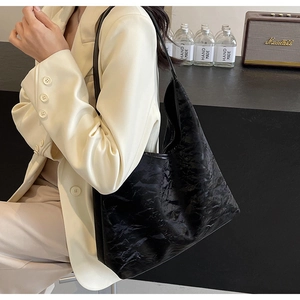 Detail of black wrinkled texture large tote bag with wide strap on a beige suit model