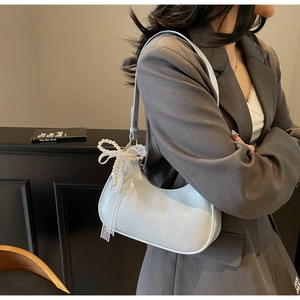 Detail der weißen glänzenden Hobo-Tasche mit abnehmbarem Perlen- und Spitzenbogen-Anhänger